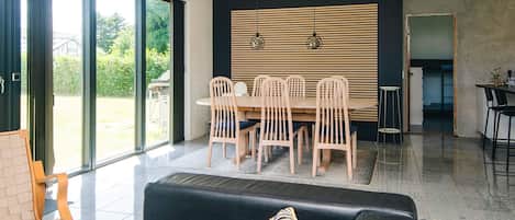A modern living room with a dining area, large sliding glass doors, and a kitchen visible through an open doorway.