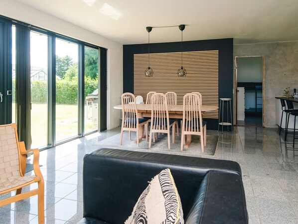 A modern living room with a dining area, large sliding glass doors, and a kitchen visible through an open doorway.