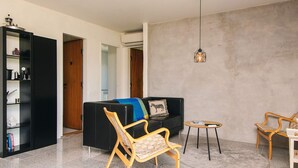 Una sala moderna con un sofá negro, una silla de madera, una mesita redonda y una estantería.