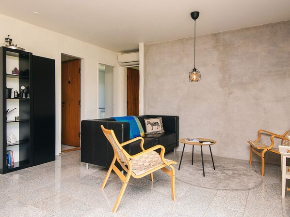 A modern living room with a black sofa, a wooden chair, a small round table, and a bookshelf.