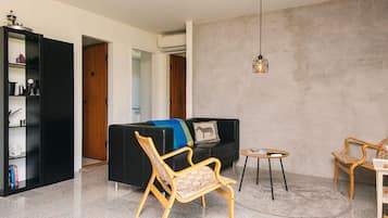 A modern living room with a black sofa, a wooden chair, a small round table, and a bookshelf.
