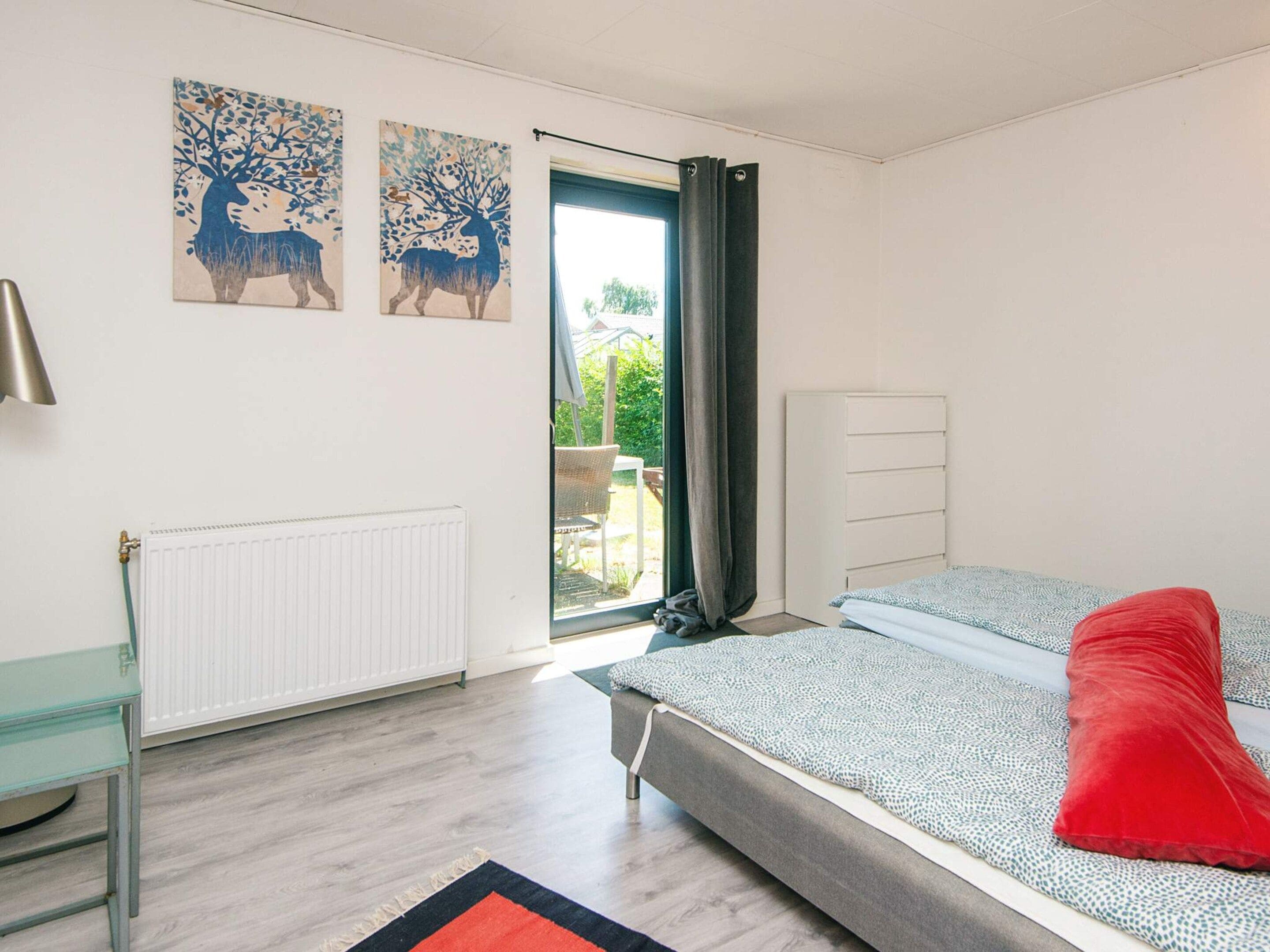 A bedroom with a bed, a radiator, a desk, and a window with curtains.