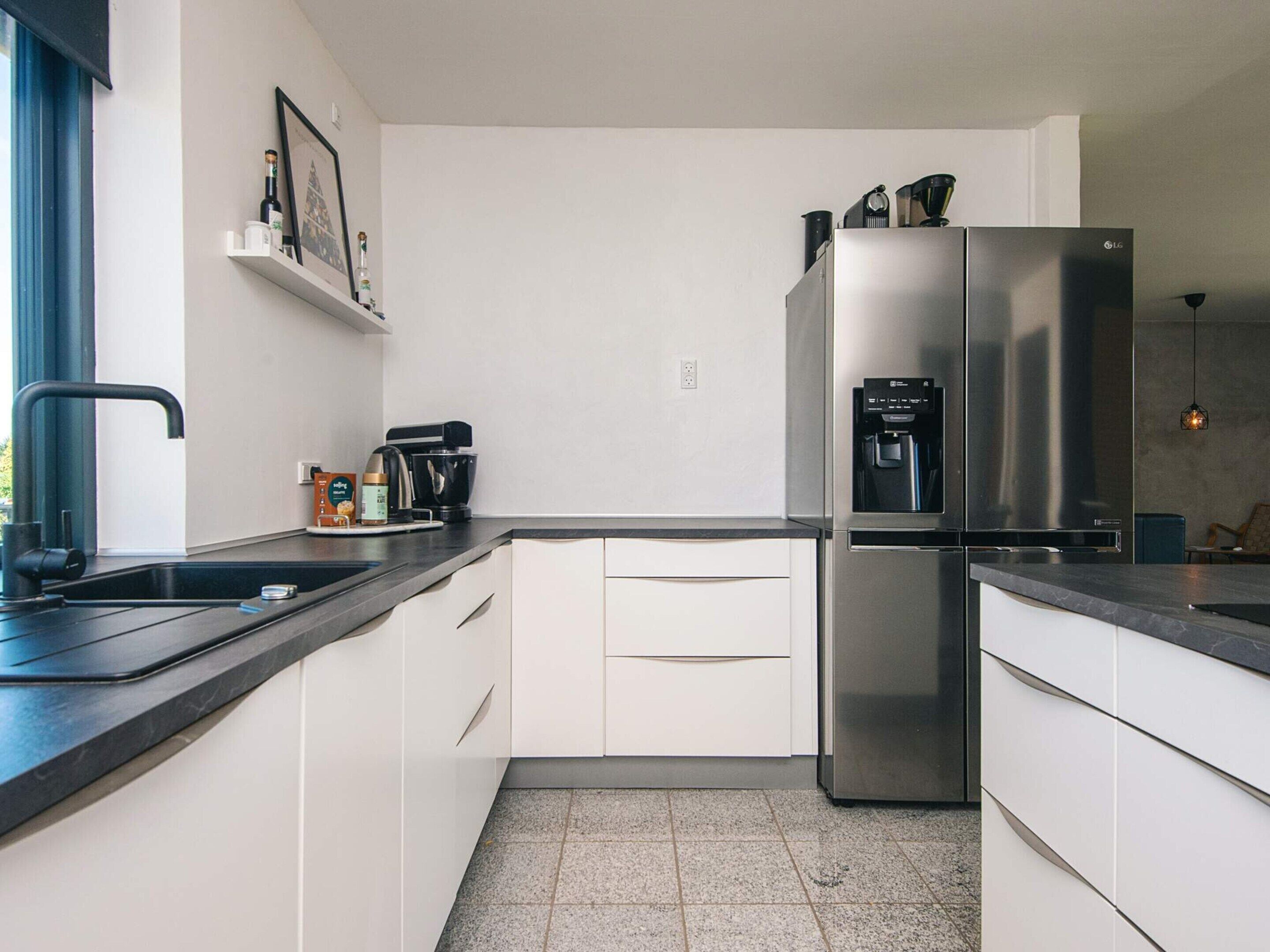 A modern kitchen with white cabinets, a stainless steel refrigerator, a coffee machine, and a water dispenser.