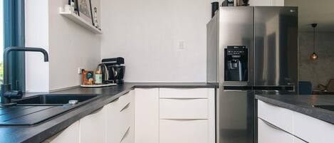 A modern kitchen with white cabinets, a stainless steel refrigerator, a coffee machine, and a water dispenser.