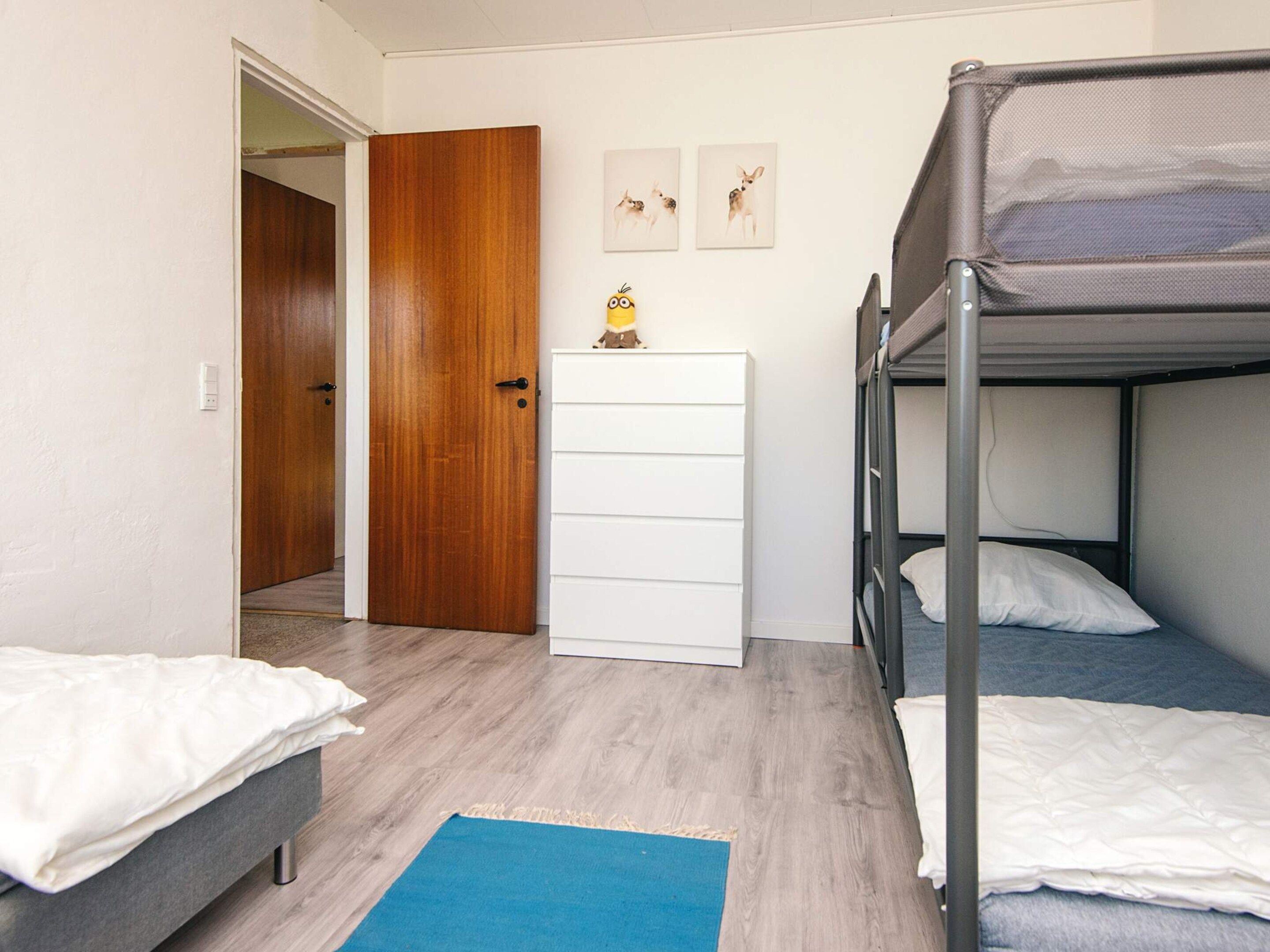 A room with a bunk bed, a white dresser, a door, and a small table with a Minion figurine.