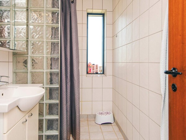 A bathroom with a white sink, a glass shower enclosure, and a small window with toiletries. - 4 Star Holiday Home in Haderslev (Haderslev)