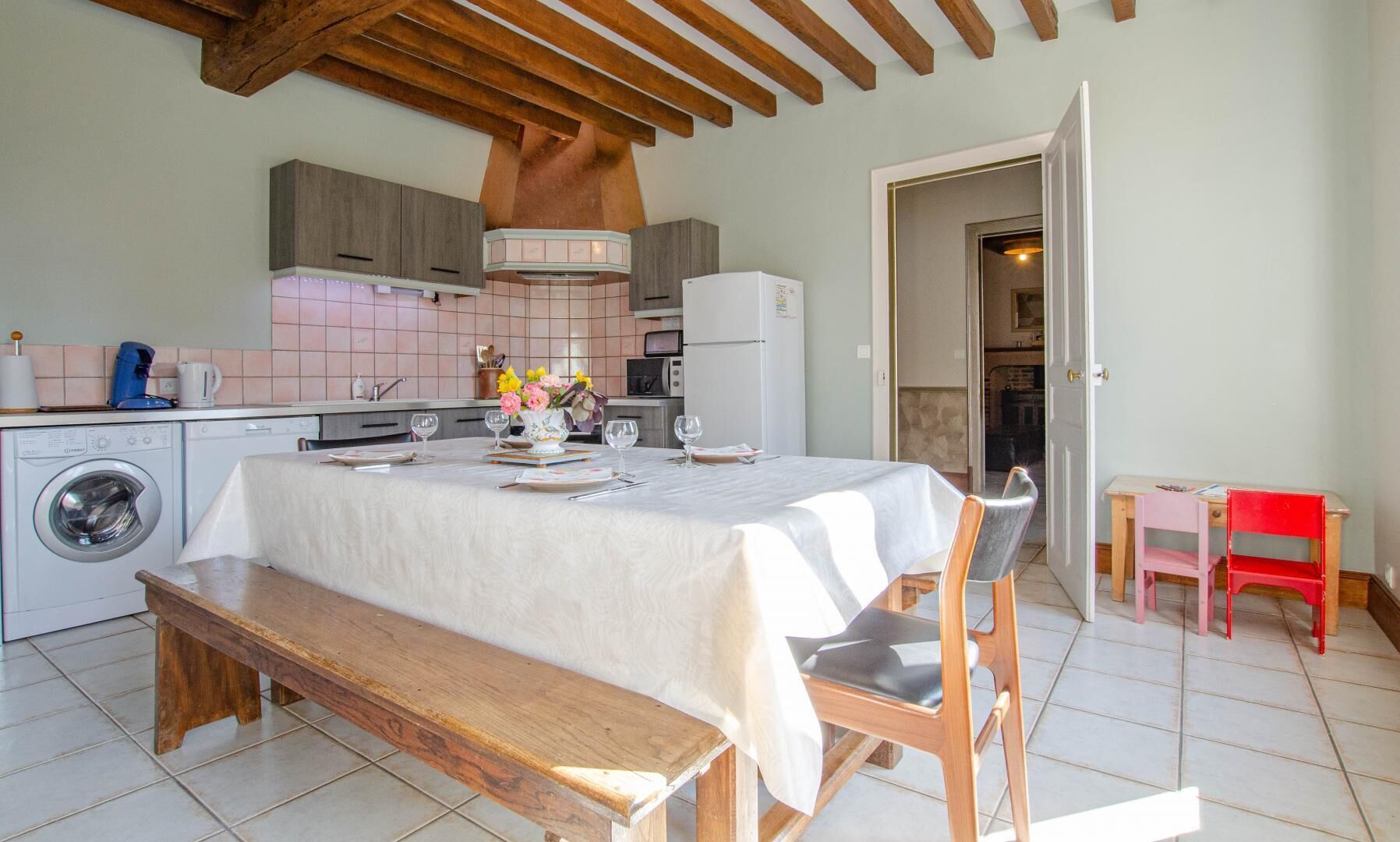 Una cocina con una mesa de comedor lista para cuatro personas, una lavadora y un banco.