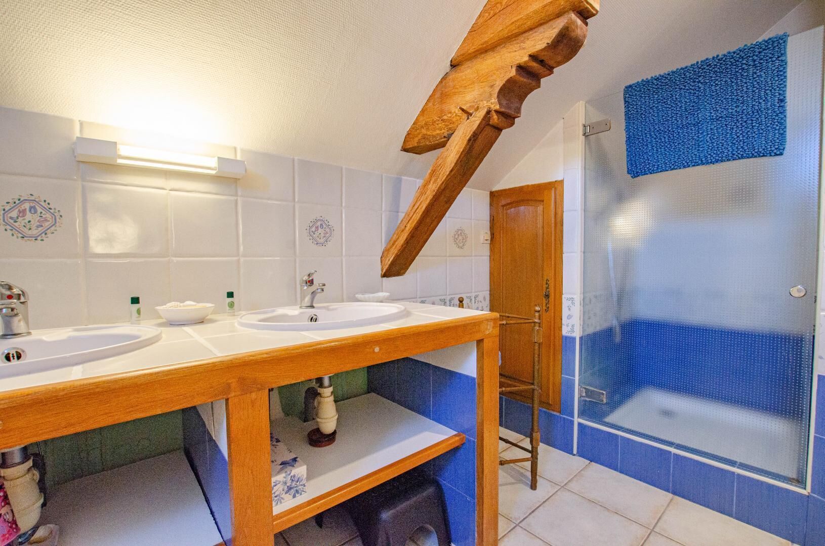 Un baño con dos lavamanos, un tocador de madera, una ducha con pared de azulejos azules y una puerta con pomo decorativo.