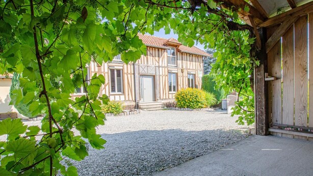 A traditional half-timbered building with a gravel driveway and a small garden with yellow flowers.