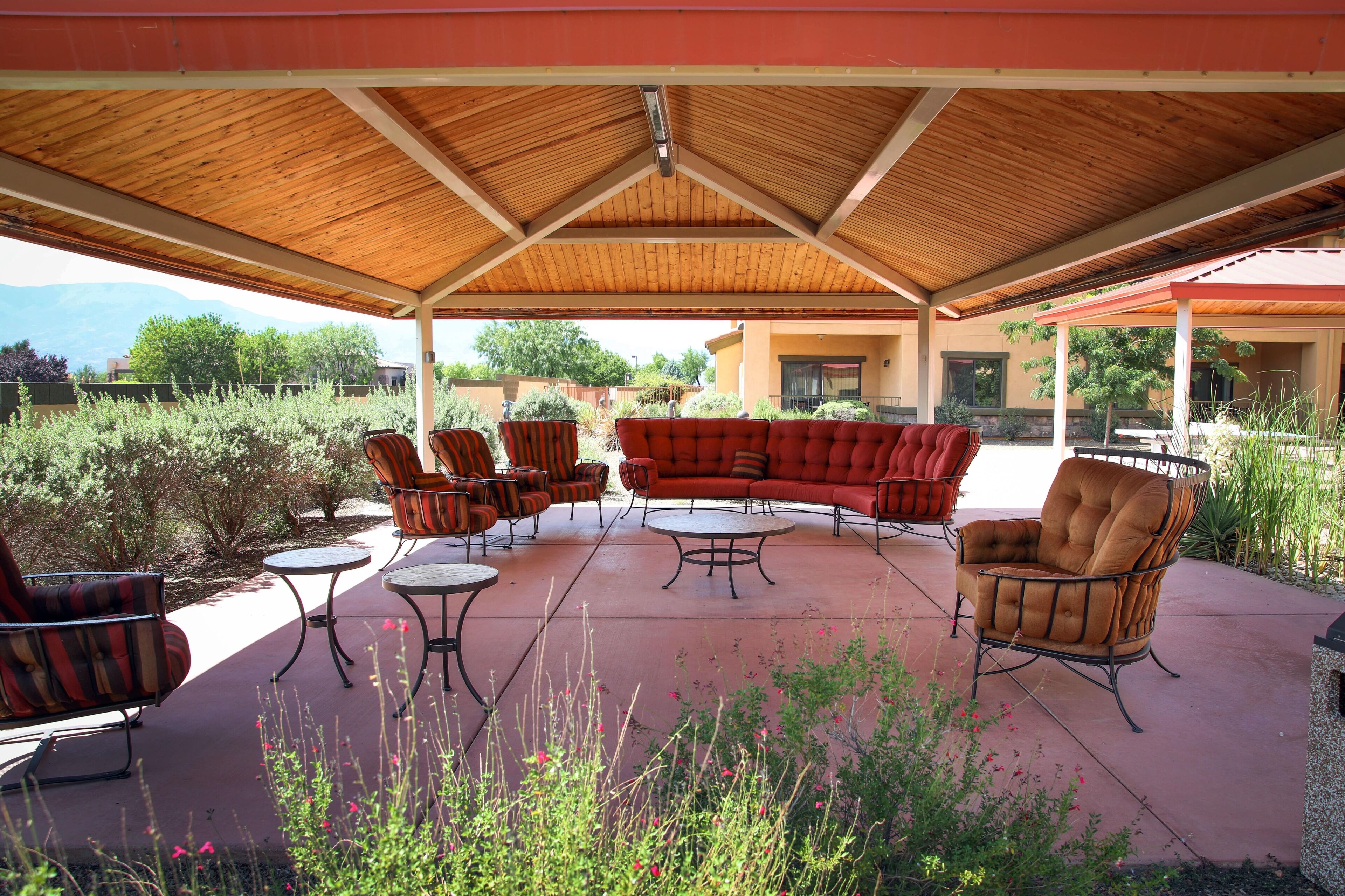 Un patio al aire libre con techo de madera, asientos con cojines rojos y pequeñas mesas redondas.