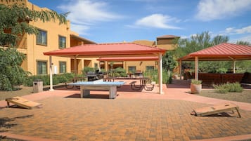 Un área de patio al aire libre con mesas de picnic, una parrilla de barbacoa y zonas de estar cubiertas.