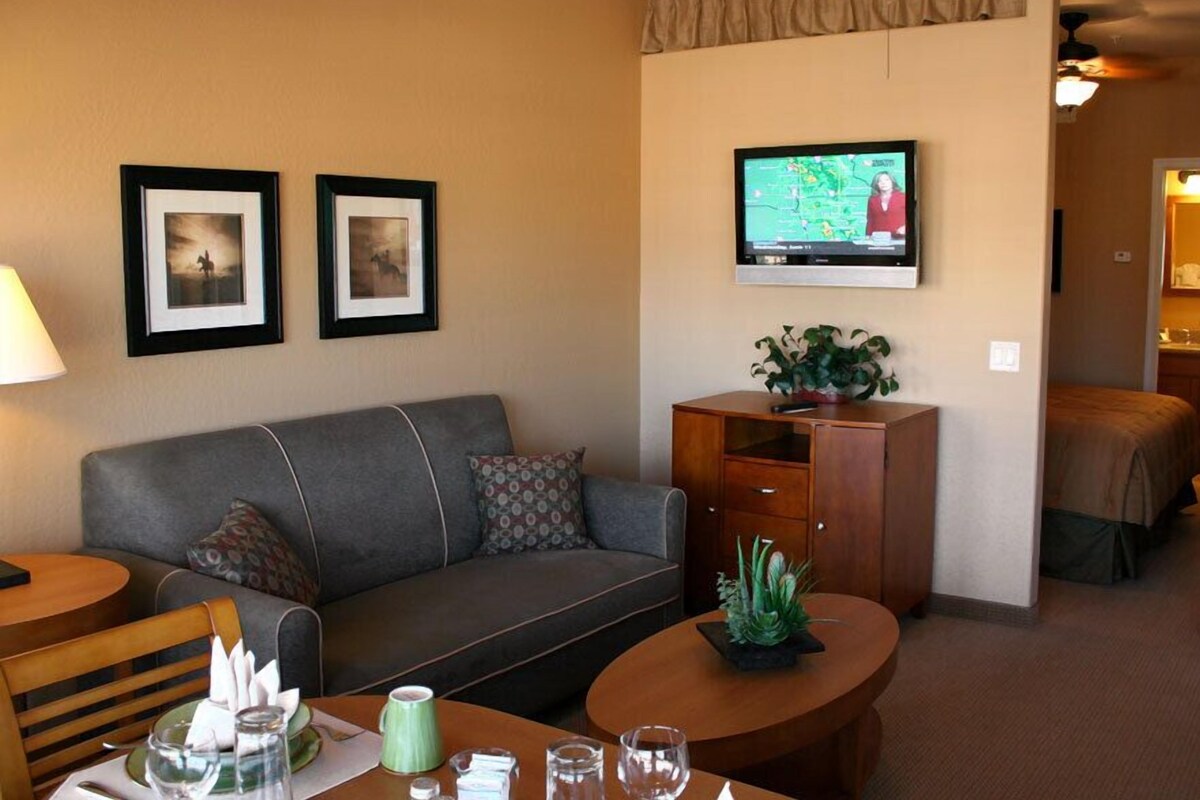 A hotel room with a sofa, a coffee table, a TV mounted on the wall, and a plant on the sideboard.