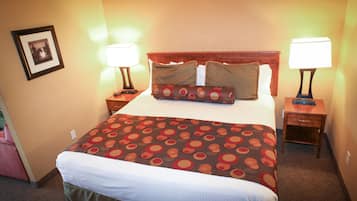 A hotel room with a large bed, two bedside tables with lamps, a framed picture on the wall, and a carpeted floor.