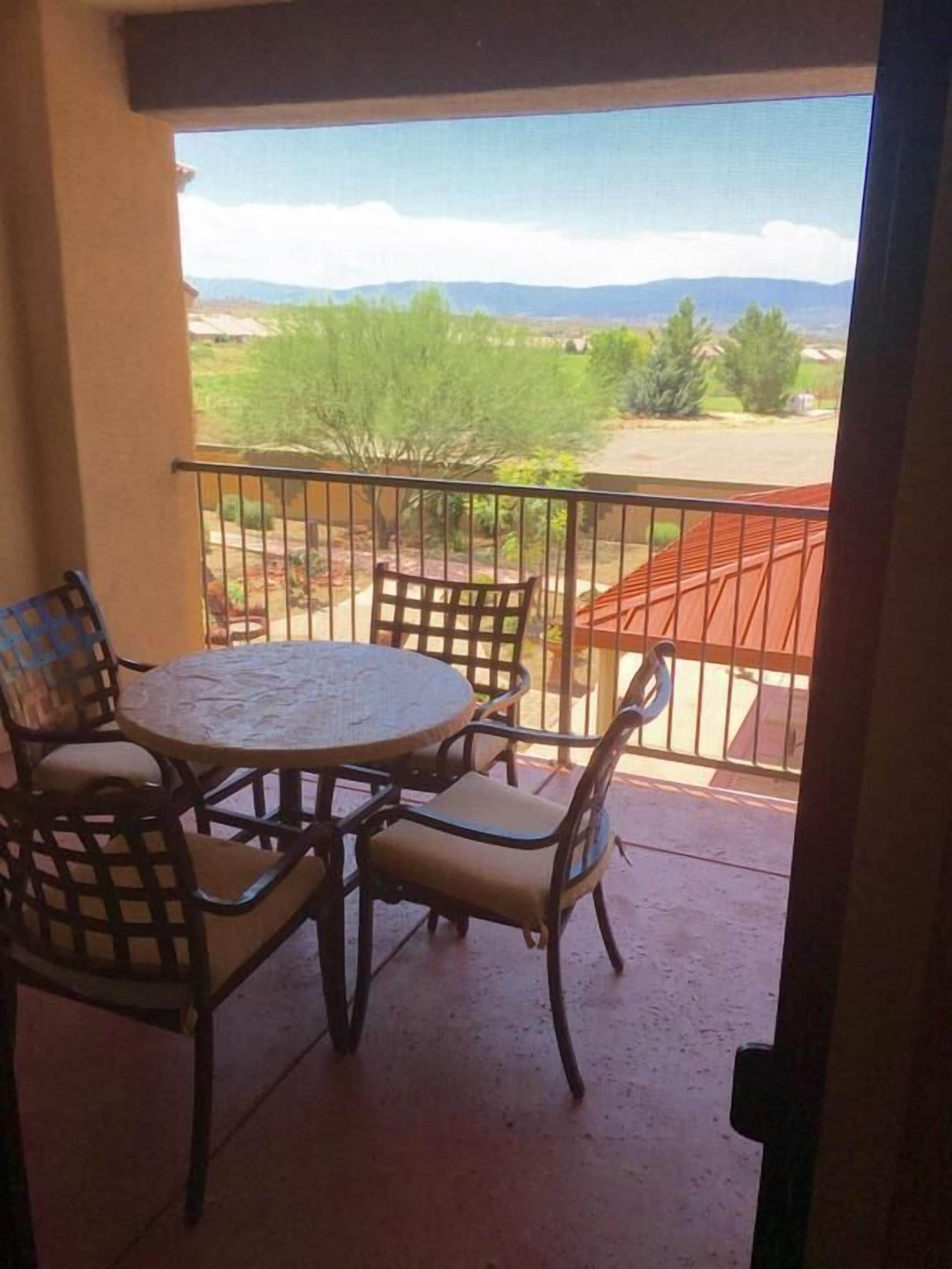Ein Balkon mit rundem Tisch und vier Stühlen, der auf eine Landschaft mit Bäumen und fernen Bergen blickt.