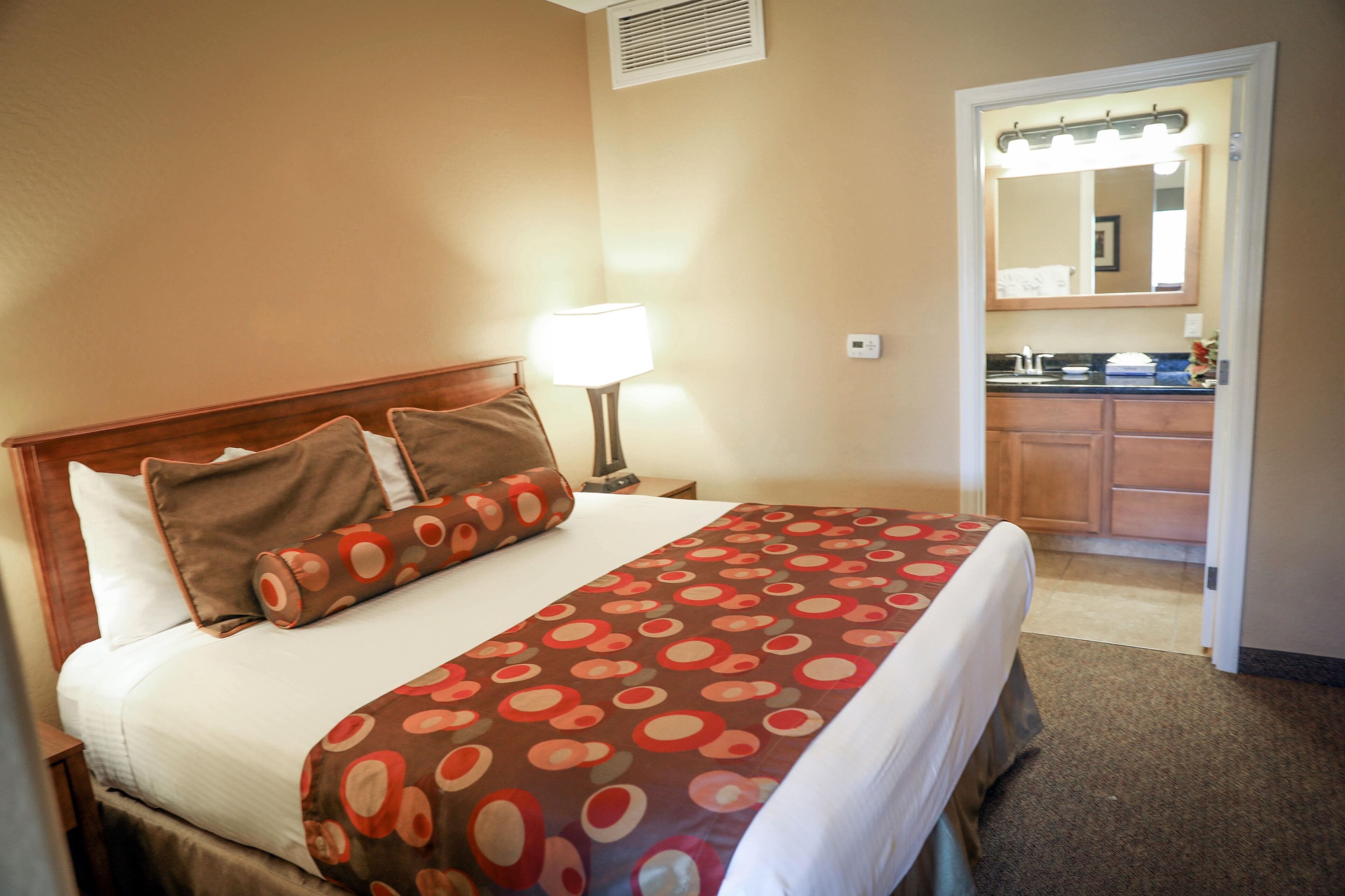 A hotel room with a neatly made bed, a bedside lamp, and a view into the bathroom.