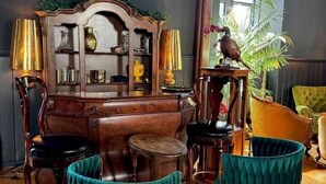 A room with a wooden coffee table, two teal armchairs, a wooden side table, and a decorative wooden cabinet with glassware. - The Old Church Isle of Bute (Rothesay)