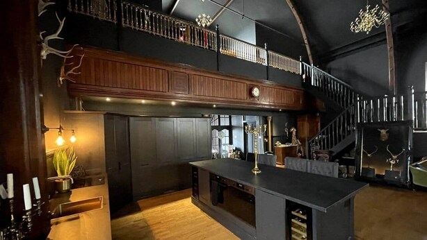 A spacious kitchen with a high ceiling, wooden cabinets, and a central island. - The Old Church Isle of Bute (Rothesay)