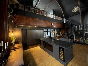 A spacious kitchen with a high ceiling, wooden cabinets, and a central island. - The Old Church Isle of Bute (Rothesay)