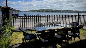 An outdoor seating area with a table and chairs, a lamp post, and a view of a body of water and distant hills. - The Old Church Isle of Bute (Rothesay)