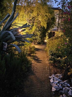 A brick pathway in a garden with various plants and a building in the background. - Two-bedroom apartment, 10 minutes from Pisa.   (Cascina)