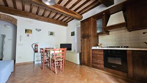 A kitchen with wooden cabinets, a tiled floor, and a dining area with chairs and a table. - A two-room apartment, 10 minutes from Pisa. (Cascina)