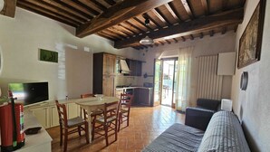 A spacious kitchen with wooden beams, a dining area with a round table and chairs, and a living area with a sofa and a television. - A two-room apartment, 10 minutes from Pisa. (Cascina)