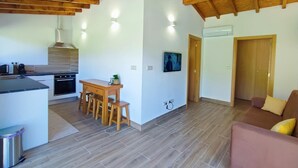 Eine moderne Küche mit Holzbalken, einem Essbereich mit Hockern, einer Couch und einem an der Wand befestigten Fernseher.