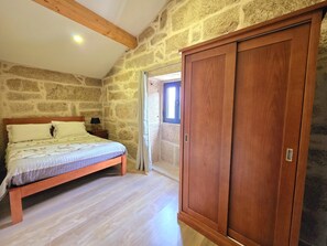 A bedroom with a wooden bed, a nightstand, a stone wall, and a wooden wardrobe. - Casa do Carvalhal | Ermida | Peneda-Gerês National Park (Ponte da Barca)