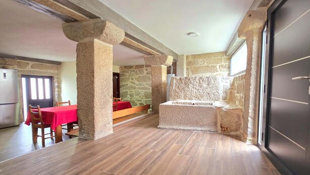 A spacious room with a stone wall, a wooden table with a red tablecloth, and a modern door.