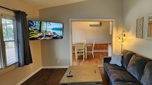 A living room with a TV, a sofa, a coffee table, and a dining area with chairs and a table.