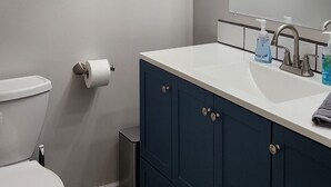 A bathroom with a toilet, a sink with a mirror, and a shower area.