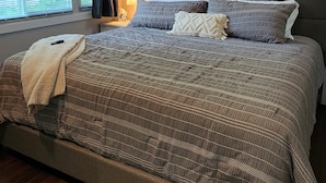 A bedroom with a large bed, a bedside table, a lamp, and an air conditioning unit.