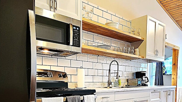 A modern kitchen with a built-in microwave, oven, and refrigerator. It features wooden flooring, white cabinets, and a wooden ceiling.