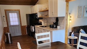 A cozy kitchen with wooden floors, white cabinets, a dining table with chairs, and a refrigerator.