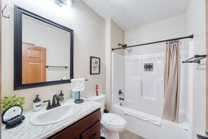 Un baño con un lavamanos blanco, un espejo grande, un inodoro y una bañera con cortina de ducha color beige.