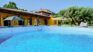 A swimming pool with a ladder, surrounded by a yellow building and trees.