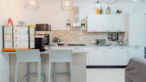 A modern kitchen with a central island, two bar stools, a built-in oven, and hanging pendant lights.