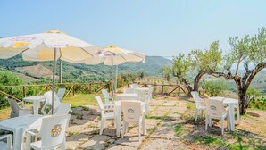 Outdoor seating with umbrellas, white plastic chairs, and a view of a hilly landscape.