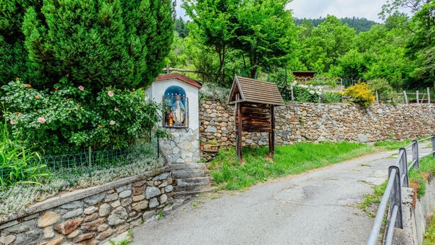 Un sentier de pierres mène à une construction rustique en bois, dotée d’un mur de pierres et d’un petit sanctuaire.