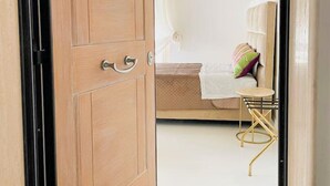 Een slaapkamer met een houten kledingkast, een bed met een witte hemel, een klein rond tafeltje en een stoel.