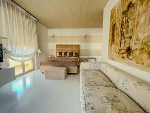 Ein Schlafzimmer mit einem Bett, einem Sofa, einem großen Gemälde und einem Fenster mit Vorhängen.