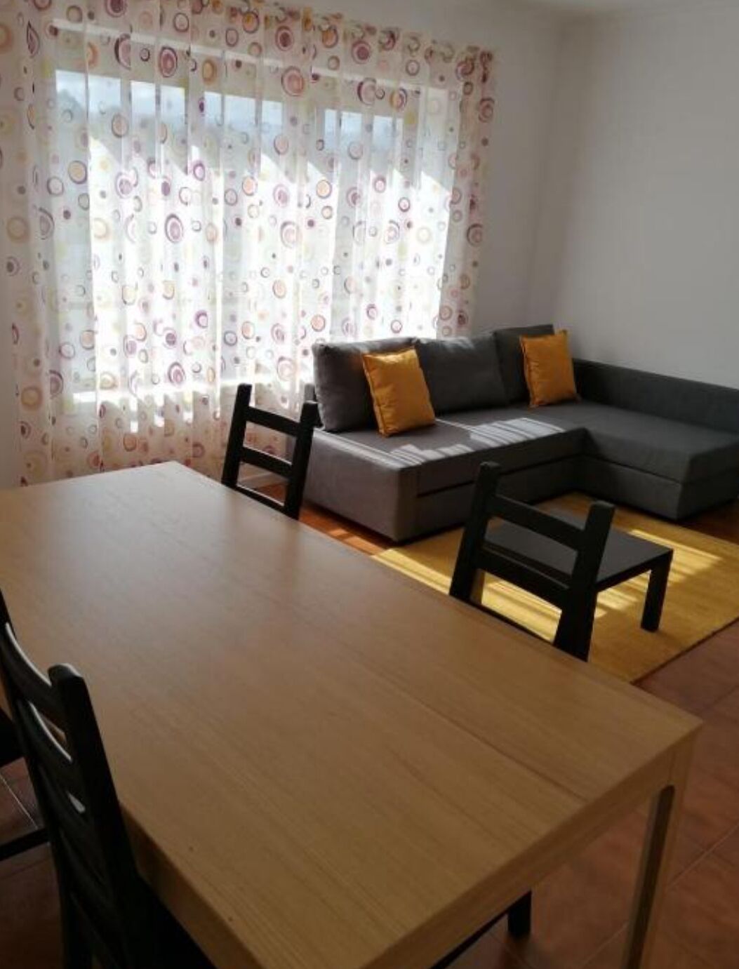 Ein Wohnzimmer mit einer Couch, zwei Sesseln, einem Holztisch und einem gemusterten Vorhang.
