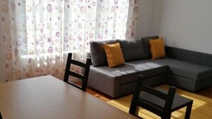 Una sala de estar con un sofá, dos sillones, una mesa de madera y una cortina estampada.