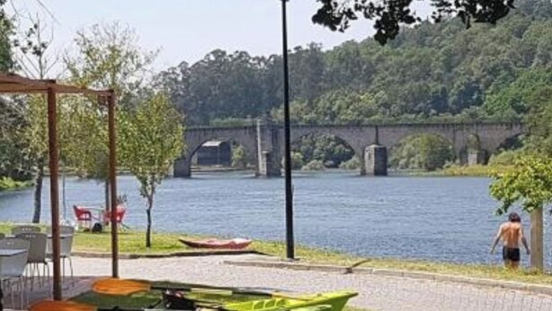 Un paisaje ribereño con una barca verde, un puente al fondo y una persona caminando.