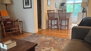 A living room with a sofa, a coffee table, and a patterned rug. There is a dining area with chairs and a table in the background. - Piermont Oasis (Piermont)