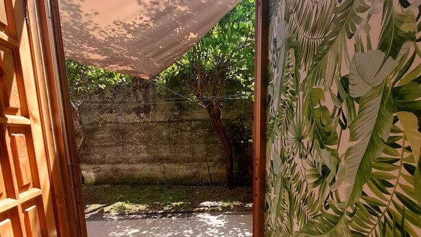 An open doorway leading to a courtyard with a tiled floor, a concrete wall, and a tree.