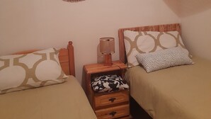 A small, cozy bedroom with two single beds, a wooden nightstand with a lamp, a mirror, and a small drawer.