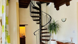 A spiral staircase in a room with a potted plant, a small table, and a cabinet with bottles.