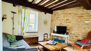 A cozy living room with a stone wall, a wooden ceiling, a sofa, a coffee table, a TV, and a chair.