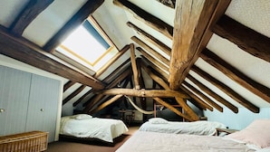 A room with a sloped ceiling, wooden beams, two beds, a small table, and a window.